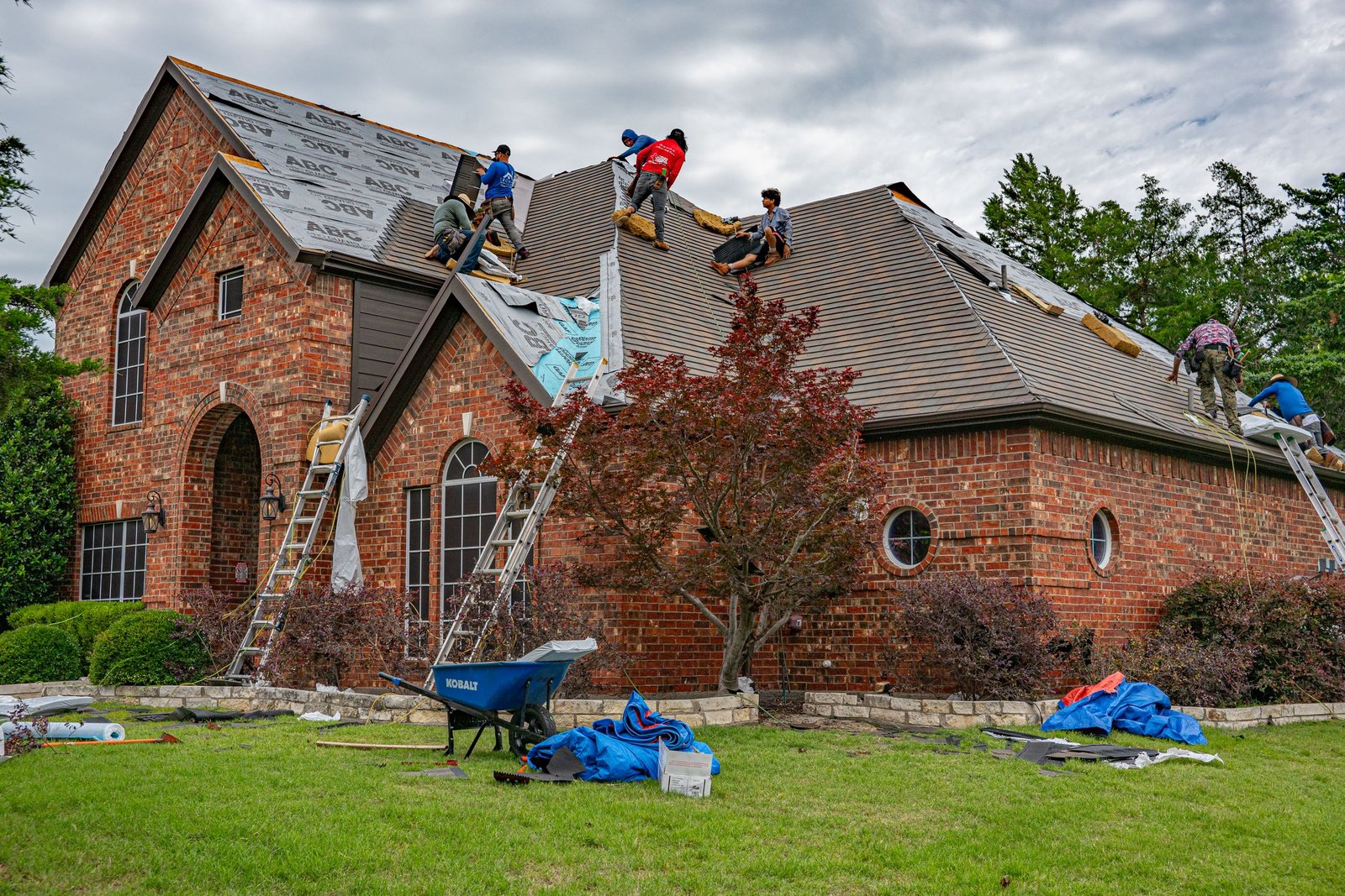 Roofers working on brick home in Allen, Texas, addressing shingles and roofing materials.